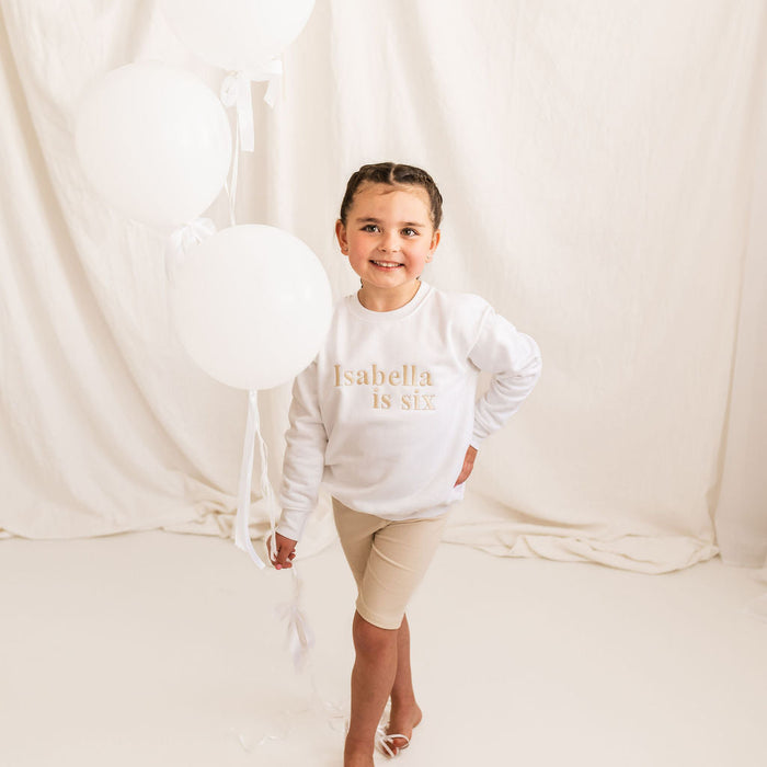 White kids age sweater with 'Isabella is six' gold lettering