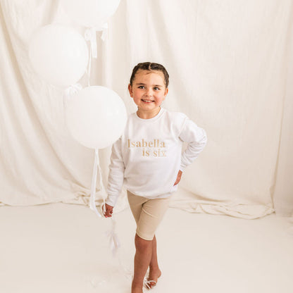 White kids age sweater with 'Isabella is six' gold lettering