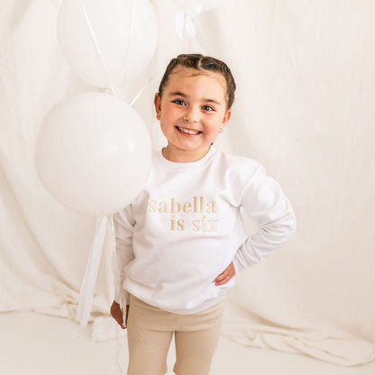 White kids age sweater with 'Isabella is six' gold lettering