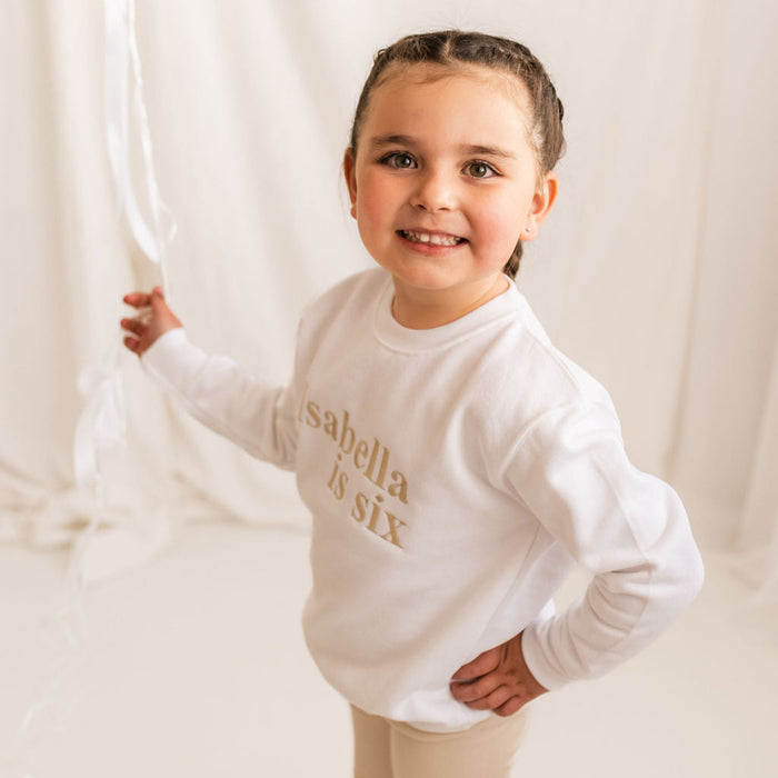 White kids age sweater with 'Isabella is six' gold lettering