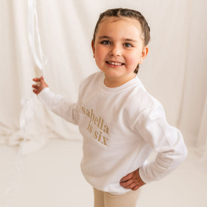 White kids age sweater with 'Isabella is six' gold lettering