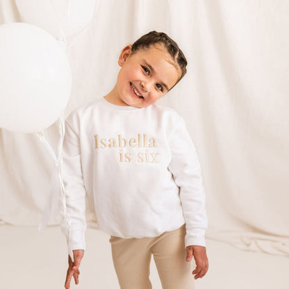 White kids birthday sweater with 'Isabella is six' gold print