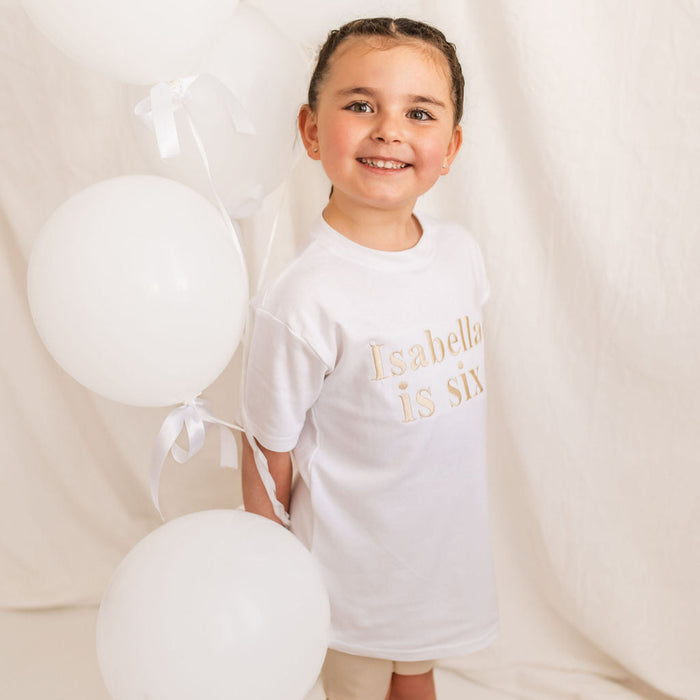 Kids white T-shirt with “Isabella is six” chest print, angled view