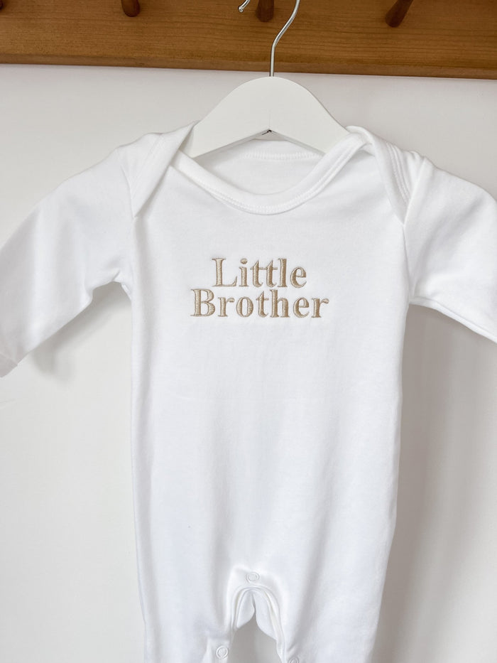 White baby sleepsuit with short sleeves and 'Little Brother' gold chest graphic