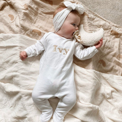 White baby romper with “Ivy” embroidered name and long sleeves; baby hugs plush toy.