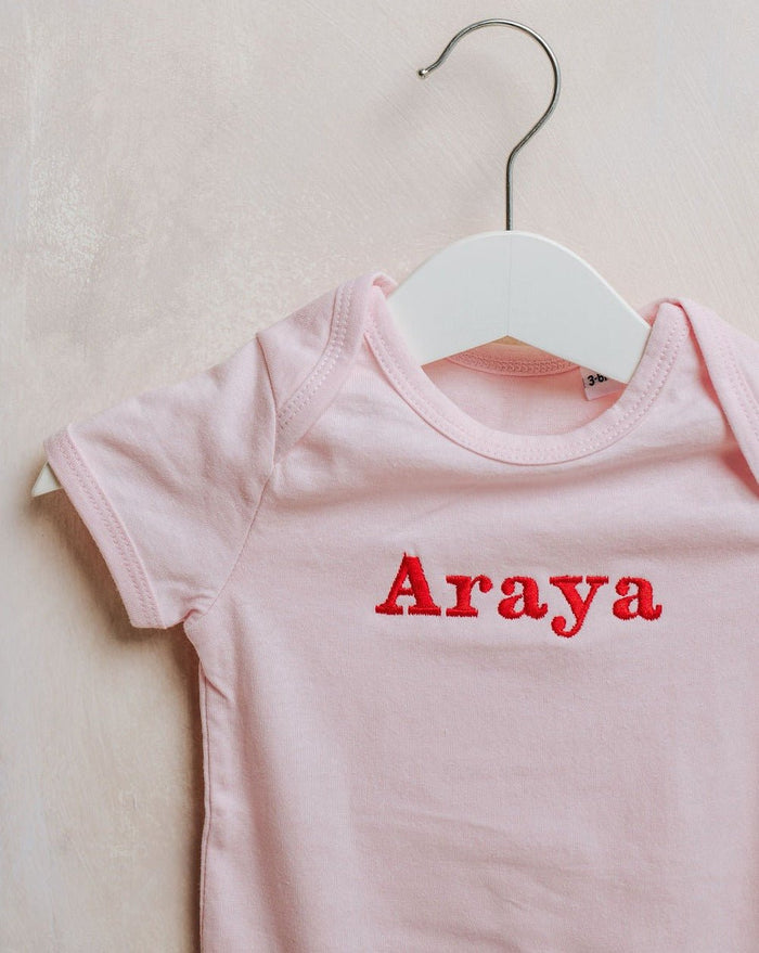 Light pink embroidered baby bodysuit close-up with Araya name