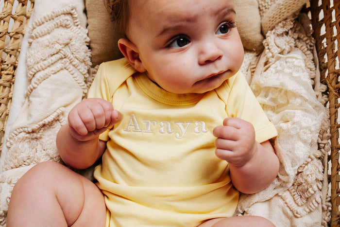 Yellow baby vest with embroidered chest text and crew neck close-up