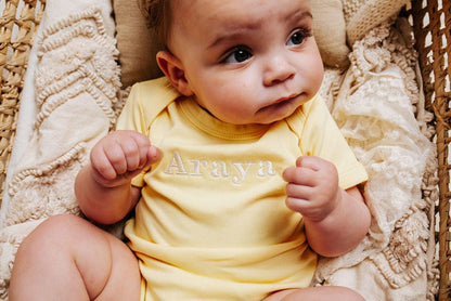 Yellow baby vest with embroidered chest text and crew neck close-up