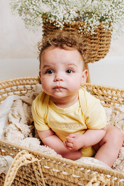 Yellow embroidered baby vest with crew neck and short sleeves on display
