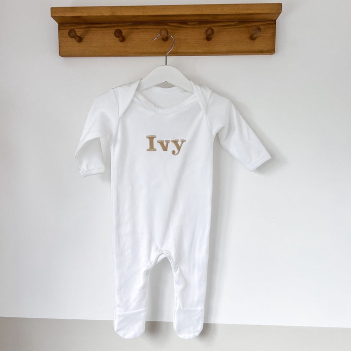 White baby romper with “Ivy” embroidered name, long sleeves, on a hanger.