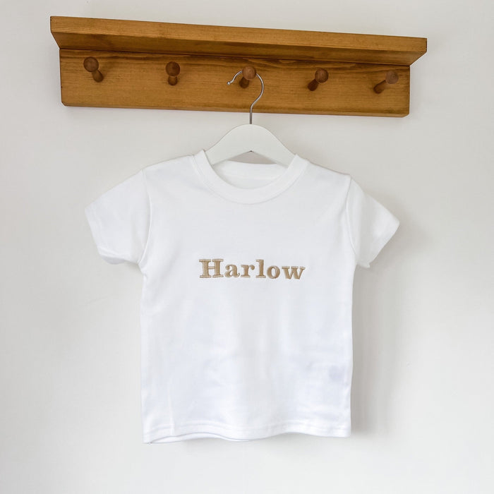 White kids T-shirt with 'Harlow' gold-tone front graphic on a hanger