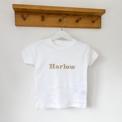 White kids T-shirt with 'Harlow' gold-tone front graphic on a hanger