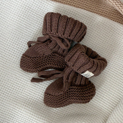 Brown knitted baby booties, ribbed cuffs with bow and small label