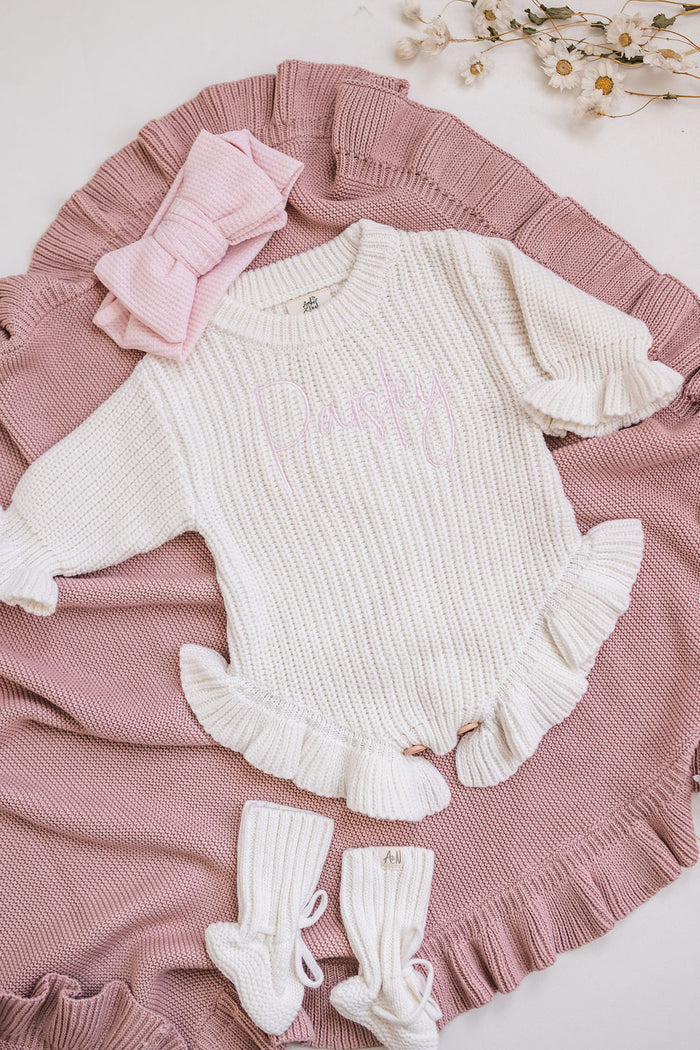 Dusty pink and white knit blanket with ruffled trim, folded over textured knit