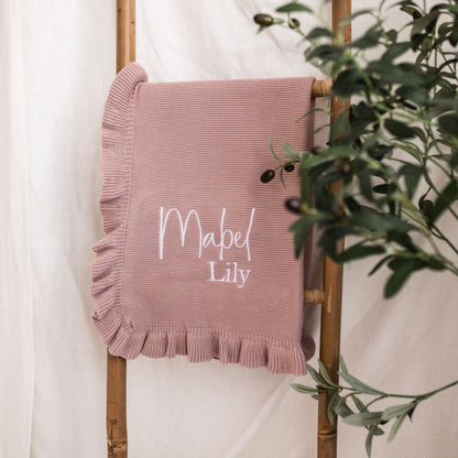 Dusty pink knit blanket with ruffled border, embroidered “Mabel Lily” on center