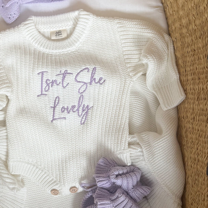 Cream knitted romper with crew neck, script 'Isn't She Lovely', purple bow on front