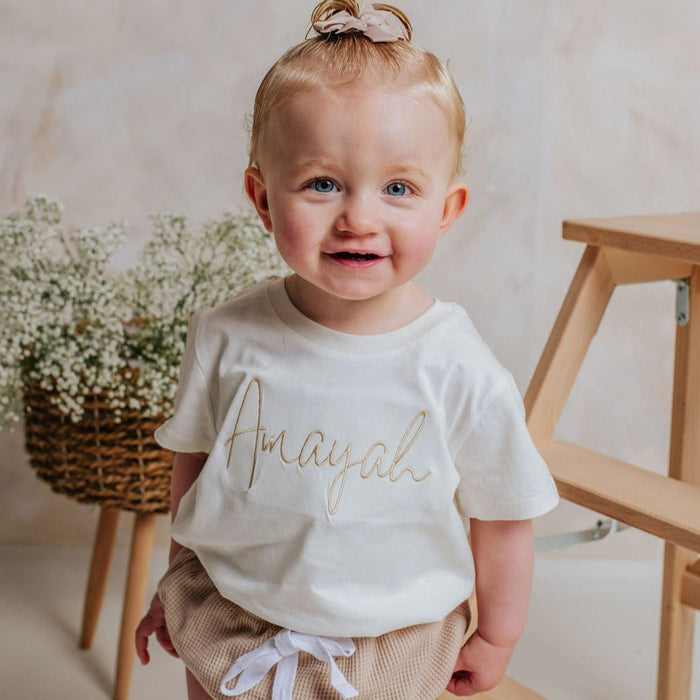 Ivory toddler T-shirt with gold script-name lettering, front view, short sleeves