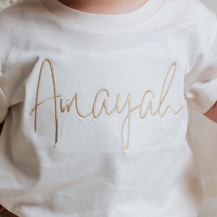 Ivory toddler T-shirt with gold embroidered script-name across the chest