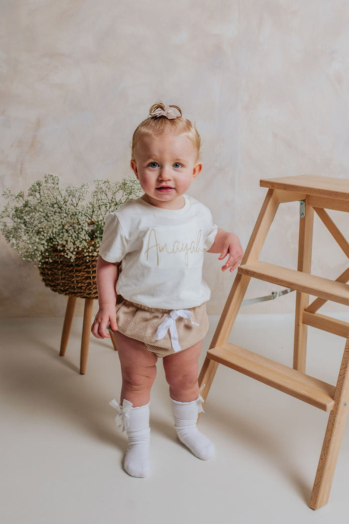 Ivory script-name toddler T-shirt with gold lettering, short sleeves