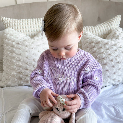 Lilac knitted baby jumper with long sleeves, embroidered script, and small floral details