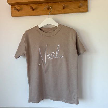 Taupe short-sleeve T-shirt with white cursive name print, crew neckline