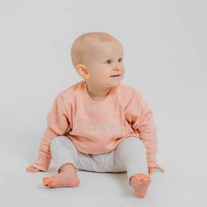 Peach baby birthday sweater with OneDerful front graphic