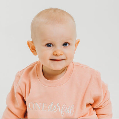 Peach baby birthday sweater with OneDerful front graphic, close-up