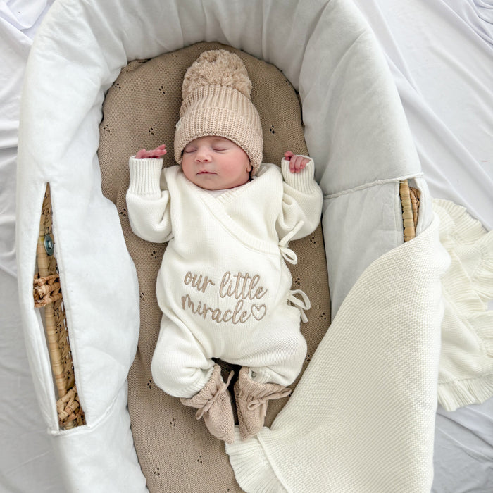 Cream knit long romper with hood-style collar, drawstring ties, “our little miracle”