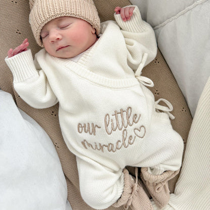 Cream baby romper close-up with “our little miracle” script and drawstring tie detail