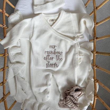 White knit baby romper with V-neck, button front, long sleeves, and ruffled pant legs