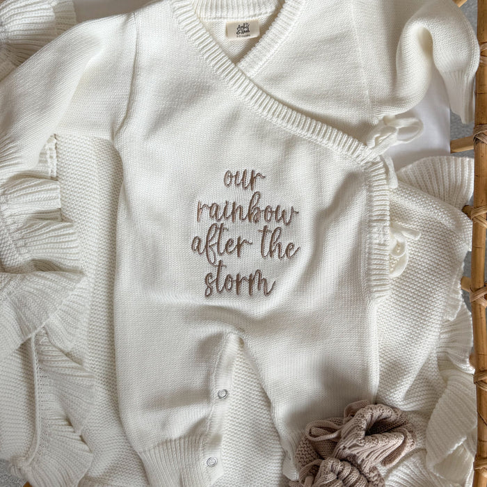 White knit baby romper with embroidered quote, button placket, and fabric rosette on leg