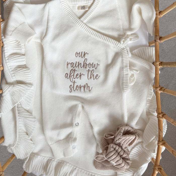 White knit baby romper with V-neck, button front, embroidered text, and fabric rosette applique