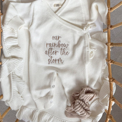 White knit baby romper with V-neck, button front, embroidered text, and fabric rosette applique