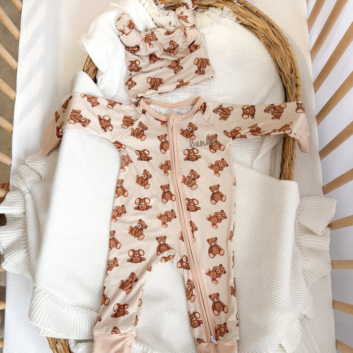 Baby zip sleepsuit laid flat, teddy bear print on cream with long zip front.