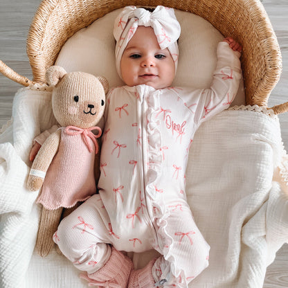 White ribbed zip sleepsuit with pink bow pattern and 'Opal' chest print, full body on baby
