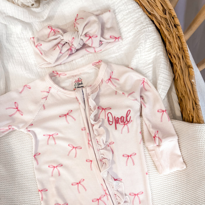 White ribbed zip sleepsuit with pink bow pattern and 'Opal' chest print, zip front