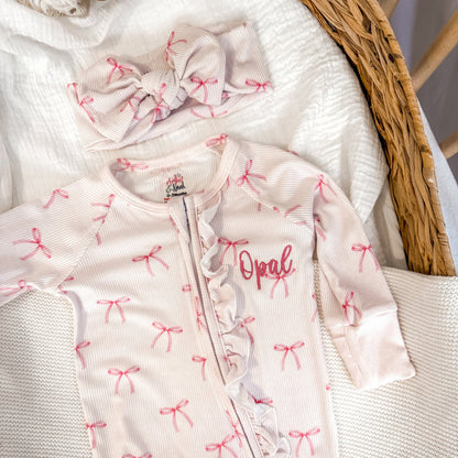 White ribbed zip sleepsuit with pink bow pattern and 'Opal' chest print, zip front