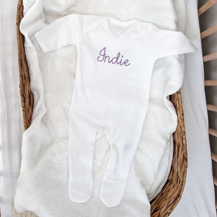 White baby sleepsuit with embroidered “Indie” on chest and long sleeves