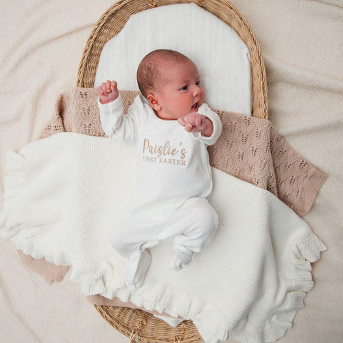 Baby wearing personalised first Easter sleepsuit in white, 'Paislie's First Easter' print