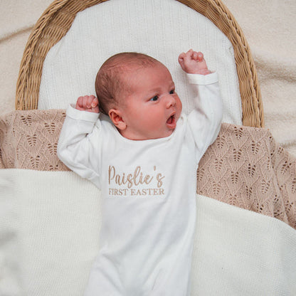 Baby wearing personalised first Easter sleepsuit in white, sleeves with 'Paislie's First Easter'