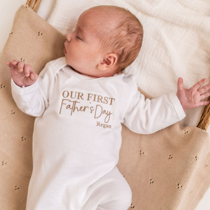 White baby sleepsuit with long sleeves, 'Our First Father's Day' logo text and Regan