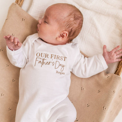 White baby sleepsuit with long sleeves, 'Our First Father's Day' logo text and Regan