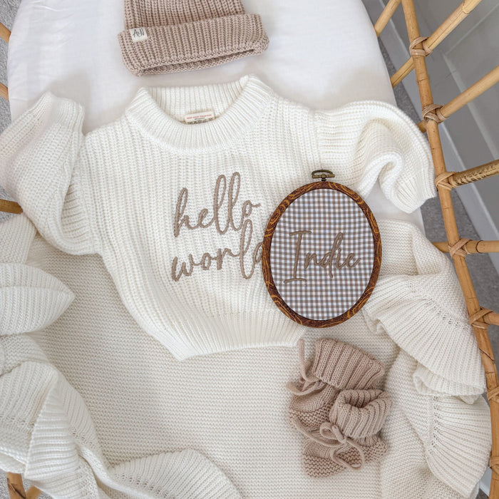 Oval baby name announcement hoop with brown trim and embroidered “Little” on gray check fabric