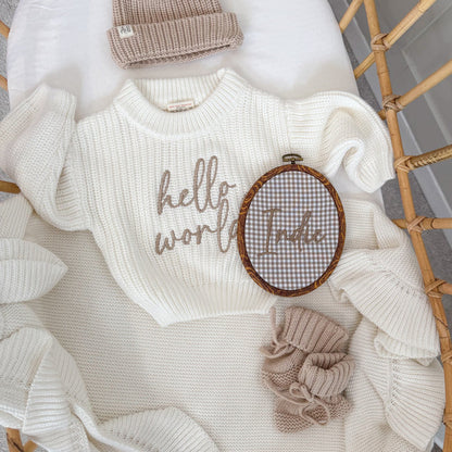 Oval baby name announcement hoop with brown trim and embroidered “Little” on gray check fabric