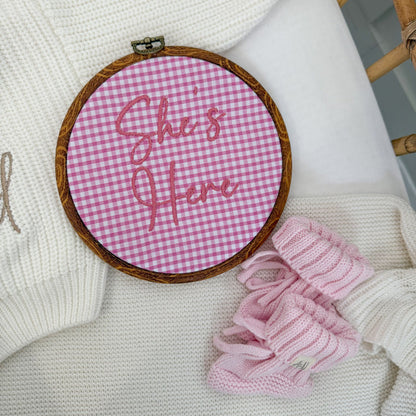 Round pink gingham baby announcement sign with stitched text: “Stella's First Date”.