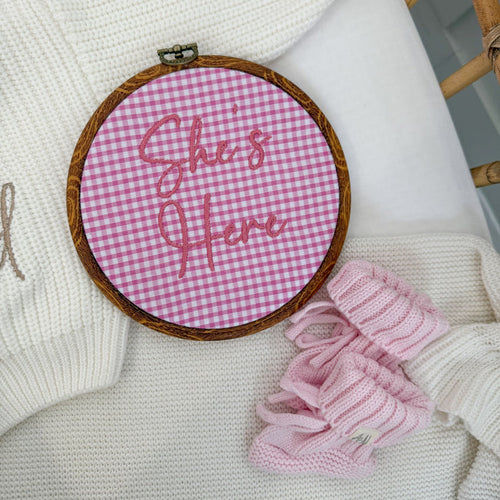 Round pink gingham baby announcement sign with stitched text: “Stella's First Date”.