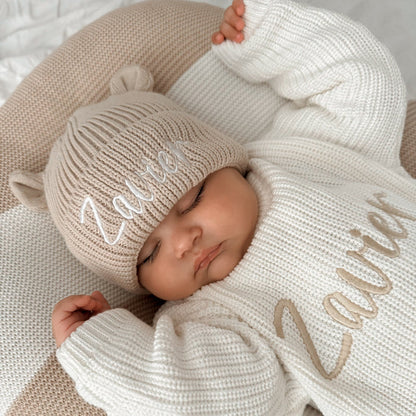 Cream knitted baby hat with bear-ear sides and embroidered name, on sleeping baby