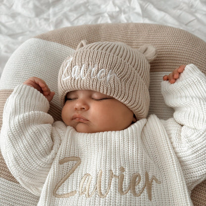 Cream knitted baby hat with bear ears and embroidered name, on sleeping newborn