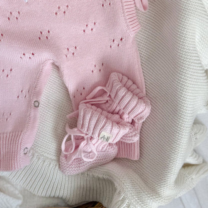 Pink knitted baby booties, bow-tied laces on a ribbed fold-over cuff