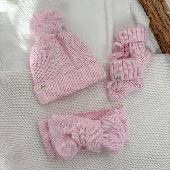 Pink knitted beanie, pink booties, and matching bow accessory set on fabric